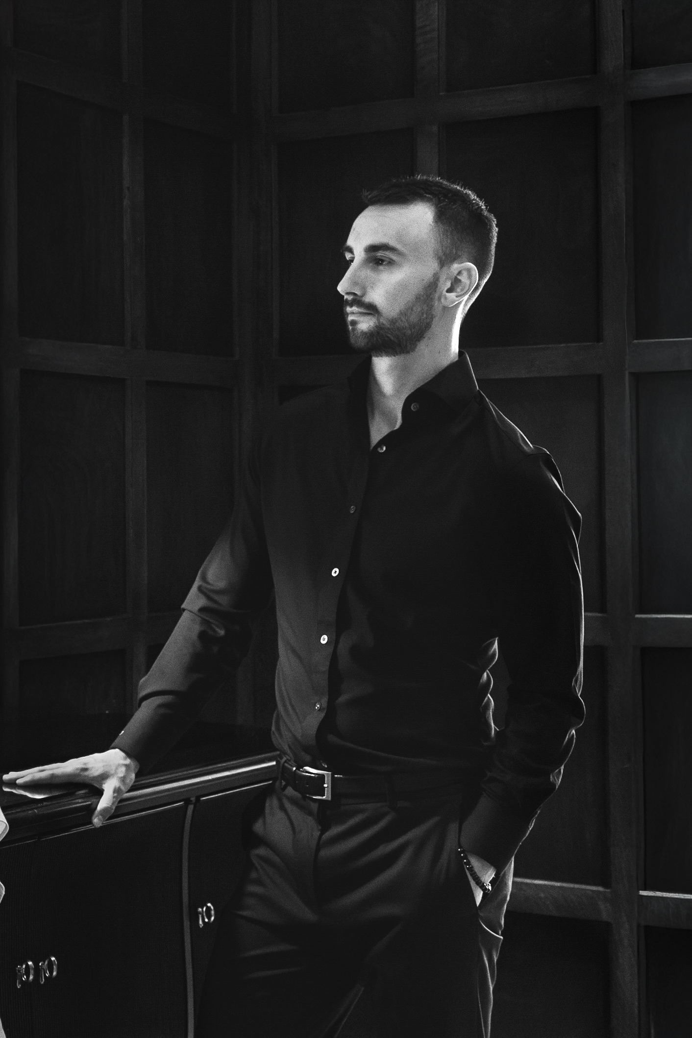 Black-and-white portrait of Kai leaning against dark wood paneling